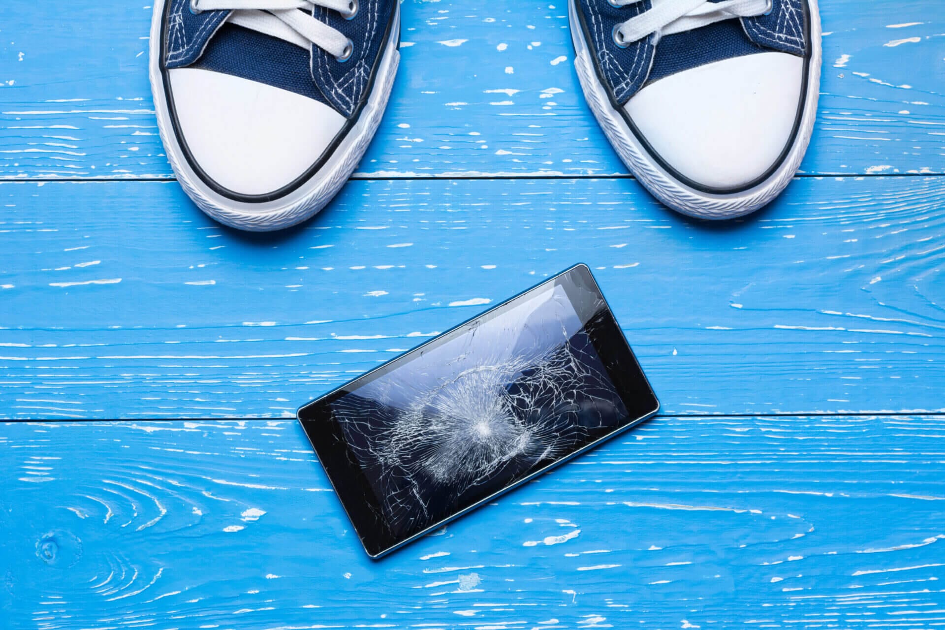 mobile phone aon a blue floor with the toes of a pair of sneakers showing