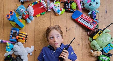 light skinned child with walkie talkie and other electrical toys arched above his head on the floor