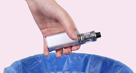 silver vape being thrown in a blue bin against a pink backdrop