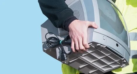 light skinned man holding a small cathode ray tube style TV. He is wearing a hi viz jacket. we cannot see his face