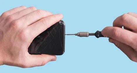 Close up of a light skinned person repairing a smart phone using a mini screwdriver.