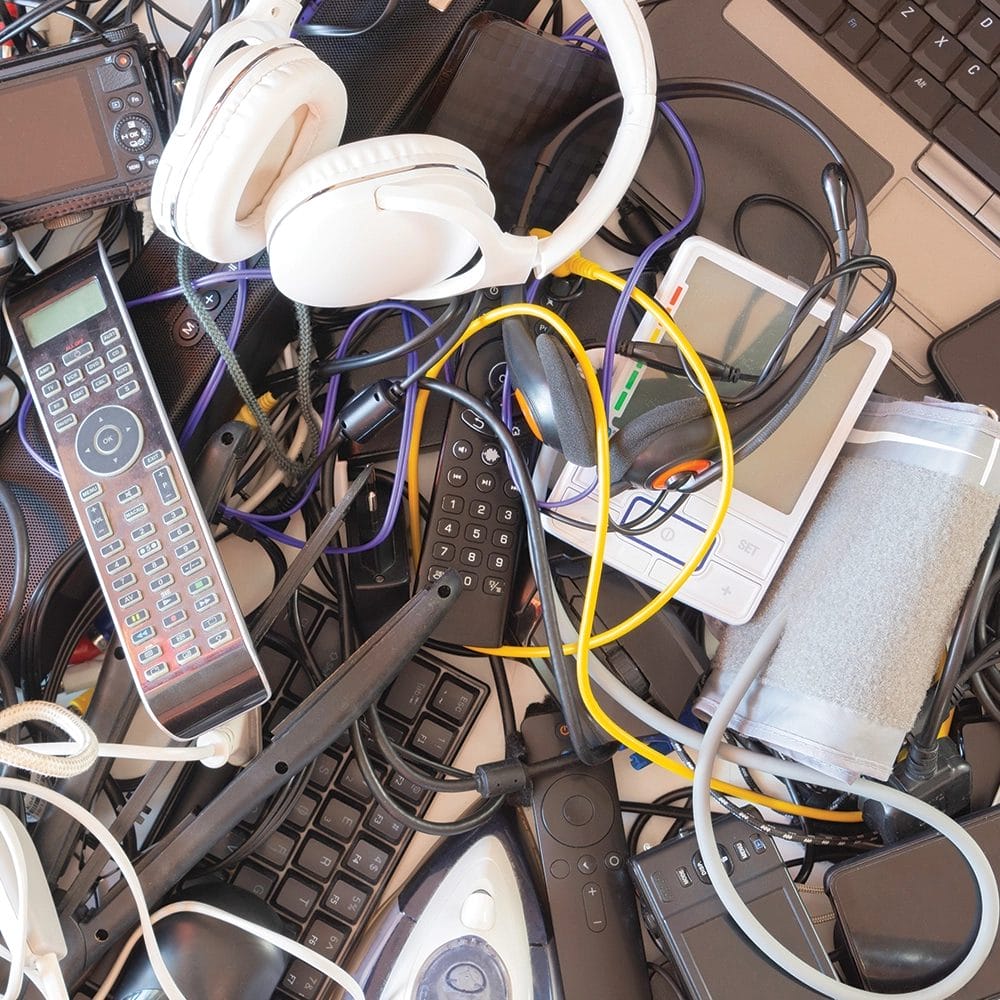 A surface covered with old electrical items including a set of white headphones, a phone and a keyboard.