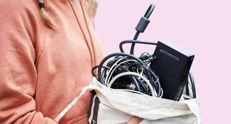 a pale skinned woman in a pink hoodie holding a cloth bag full of electrical items