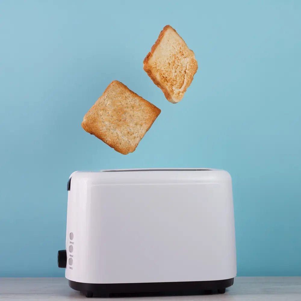 a white toaster with two slices of golden white toast popping out of it in mid air against a blue wall