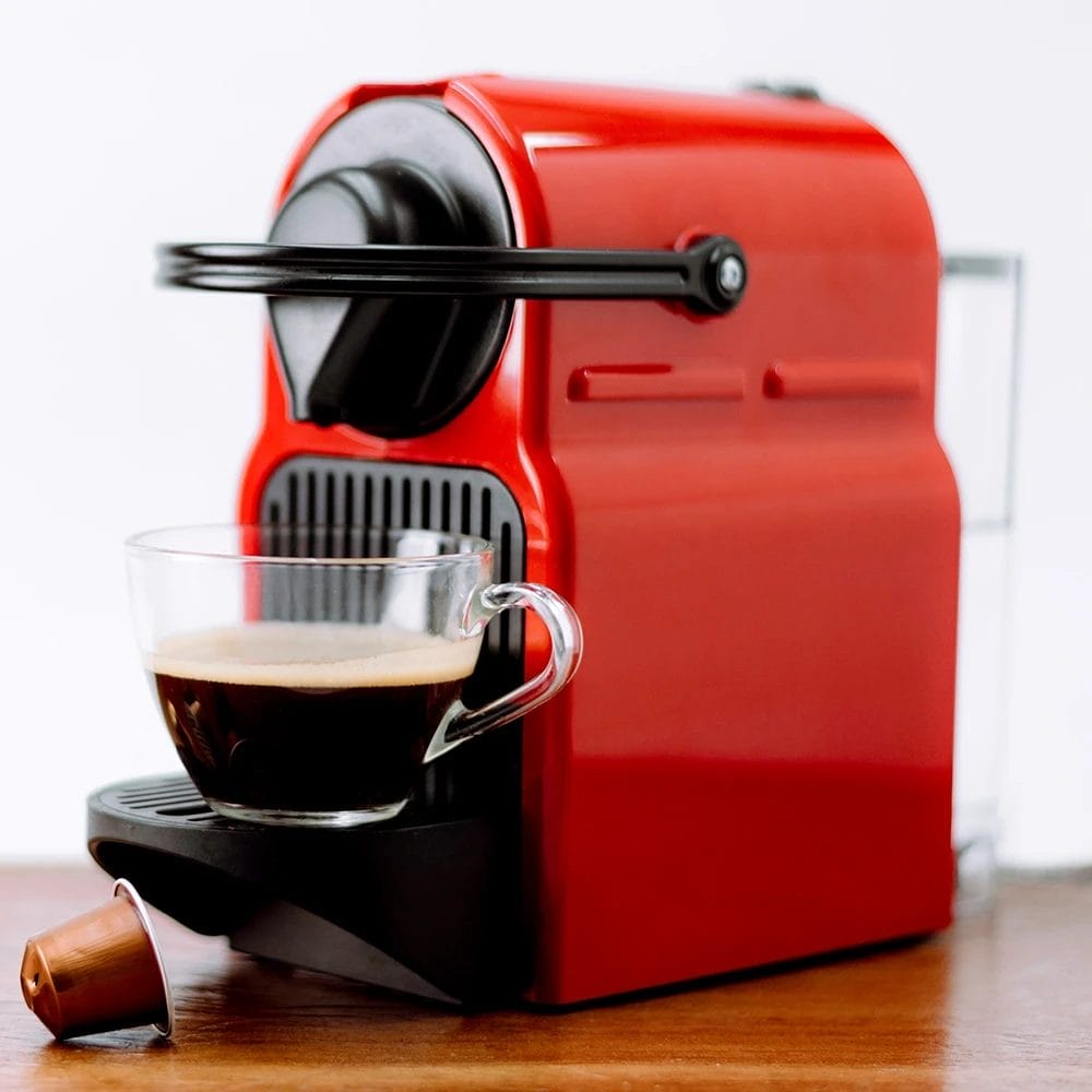 red domestic coffee machine with pods and half full glass coffee cup